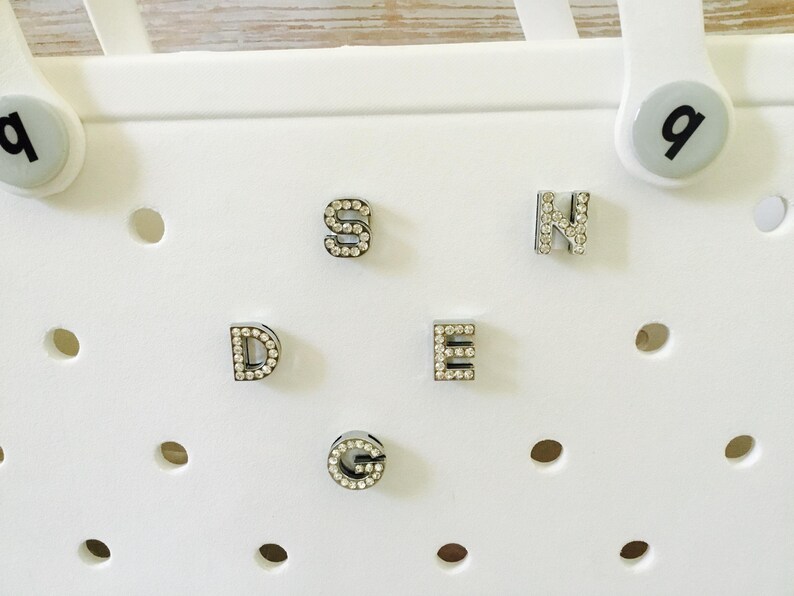 Peut inclure: Cinq lettres blanches avec des strass qui &eacute;pellent le mot "SDEG" sur un fond blanc.