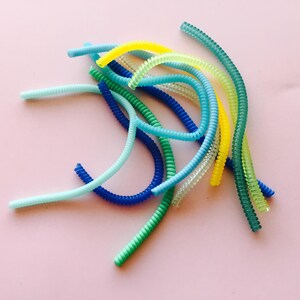 May include: A collection of colorful, coiled plastic cords in shades of blue, green, and yellow. The cords are arranged in a loose pile on a pink background.