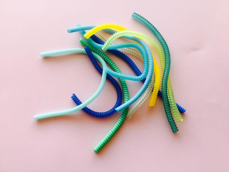 May include: A collection of colorful, coiled plastic cords in shades of blue, green, and yellow. The cords are arranged in a loose pile on a pink background.