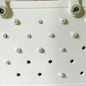 May include: White tote bag with a perforated design and white pearl embellishments.