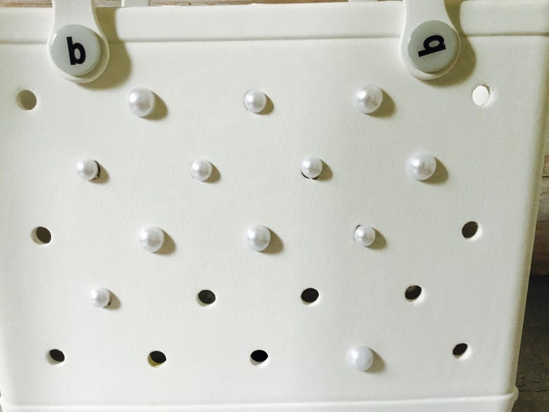 May include: White tote bag with a perforated design and white pearl embellishments.