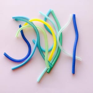 May include: A collection of colorful, coiled plastic cords in shades of blue, green, and yellow. The cords are arranged in a random pattern on a white background.