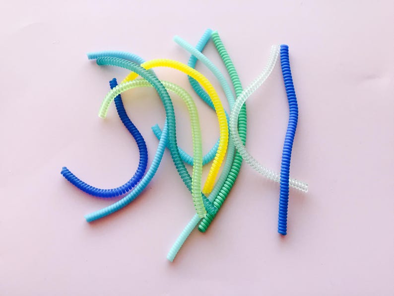 May include: A collection of colorful, coiled plastic cords in shades of blue, green, and yellow. The cords are arranged in a random pattern on a white background.