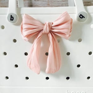 May include: White tote bag with a pink bow on the front. The bag has a  "b" on one handle and a "d" on the other handle.