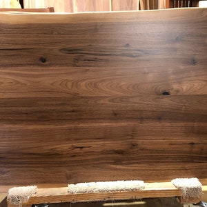 May include: A large, rectangular slab of dark brown wood with a live edge. The wood has a natural, rustic finish and shows the grain pattern of the wood.