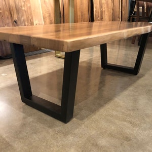 May include: A wooden coffee table with a live edge top and black metal legs. The table has a natural wood finish and is supported by four legs.