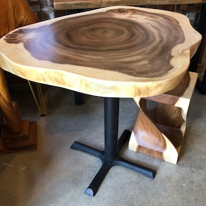 May include: A wooden table with a live edge top and a black metal base. The table is round and has a natural wood finish. The table is paired with a matching wooden stool with a unique, twisted design.