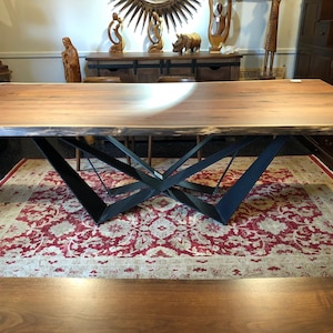 May include: A large wooden dining table with a live edge top and a black metal base. The table is sitting on a red and cream patterned rug.