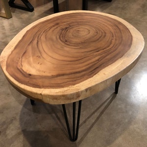 May include: A round wooden coffee table with a natural wood grain finish and black hairpin legs. The table top is a thick slice of wood with a natural edge.
