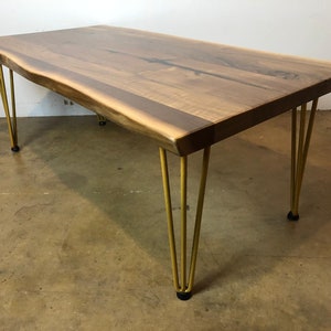 May include: A live edge walnut wood table with a natural wood finish and gold hairpin legs. The table has a rustic, modern design.