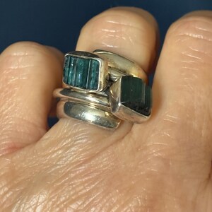 Peut inclure: Une bague en argent avec trois bandes et deux pierres pr&eacute;cieuses vertes. Les pierres pr&eacute;cieuses sont rectangulaires et pr&eacute;sentent un motif stri&eacute;.