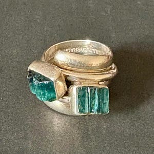 Peut inclure: Une bague en argent avec trois bandes et deux pierres pr&eacute;cieuses vertes. La bague est empil&eacute;e avec les bandes qui se chevauchent.