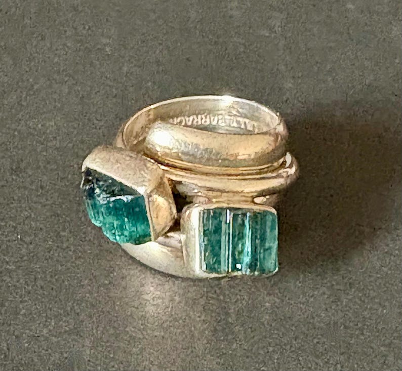 Peut inclure: Une bague en argent avec trois bandes et deux pierres pr&eacute;cieuses vertes. La bague est empil&eacute;e avec les bandes qui se chevauchent.