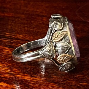 May include: A silver ring with a large, faceted amethyst gemstone set in a leafy design. The leaves are accented with gold.