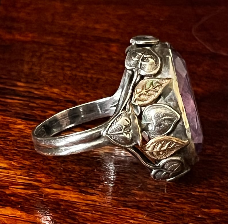 May include: A silver ring with a large, faceted amethyst gemstone set in a leafy design. The leaves are accented with gold.