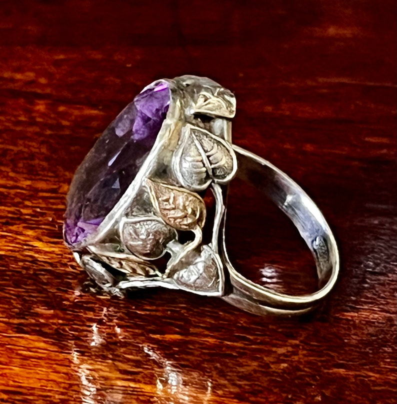 May include: A silver ring with an amethyst gemstone set in a leaf design.