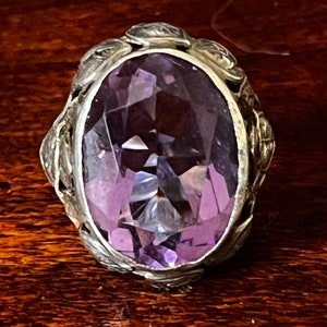 May include: A silver ring with an oval-shaped amethyst gemstone set in a detailed floral design.