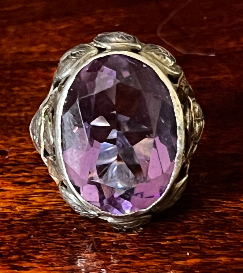May include: A silver ring with an oval-shaped amethyst gemstone set in a detailed floral design.