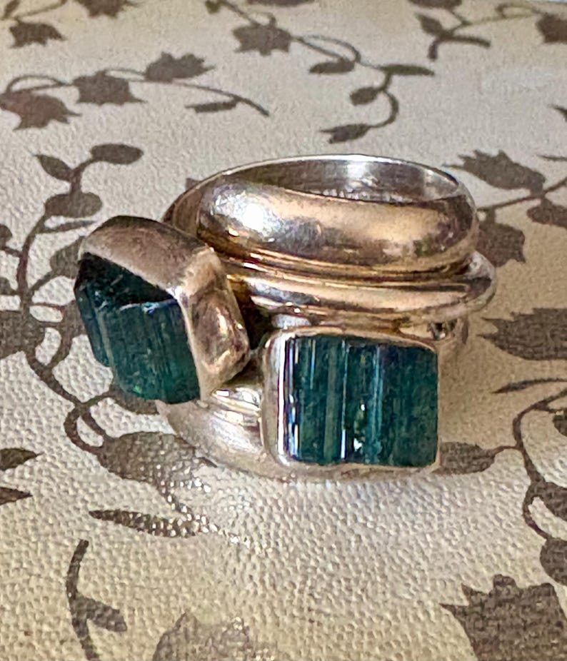 Peut inclure: Une bague en argent avec plusieurs bandes et deux pierres pr&eacute;cieuses vertes.