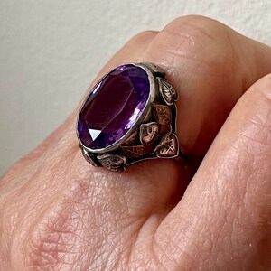May include: A silver ring with a large, oval-shaped amethyst gemstone set in a leafy design.