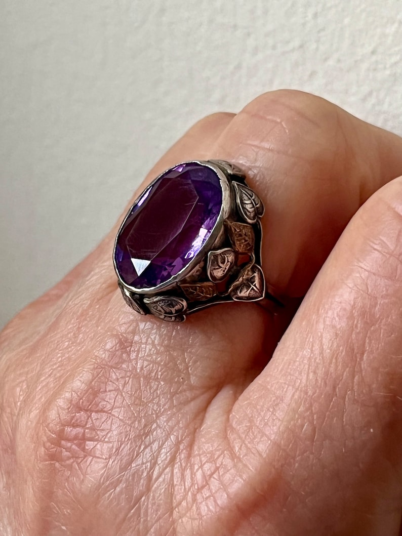 May include: A silver ring with a large, oval-shaped amethyst gemstone set in a leafy design.