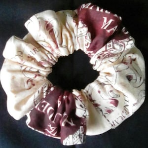 May include: A white and burgundy fabric hair scrunchie with a print of a book cover. The book cover has the text "MARAUDERS" printed on it.