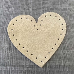 May include: A beige heart-shaped piece of leather with holes punched around the edge.