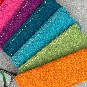 以下が含まれることがあります： ピンク、パープル、ティール、ブルー、グリーン、オレンジなど、さまざまな色合いのフェルト製の眼鏡ケースのセットです。ケースは白いステッチで縁取られており、柔らかくふわふわした質感です。