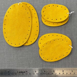 May include: Four yellow oval-shaped leather patches with holes around the edges. The patches are stacked in pairs.