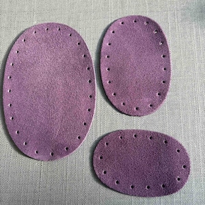 May include: Three purple suede leather patches with stitching around the edges and holes for sewing. The patches are oval shaped and come in three different sizes.