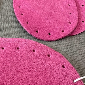 May include: Three pink suede leather patches with holes punched around the edges. The patches are for crafting and sewing projects.
