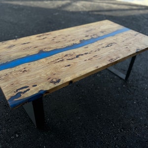 May include: A wooden table with a blue resin river running through the center. The table has a black metal frame.