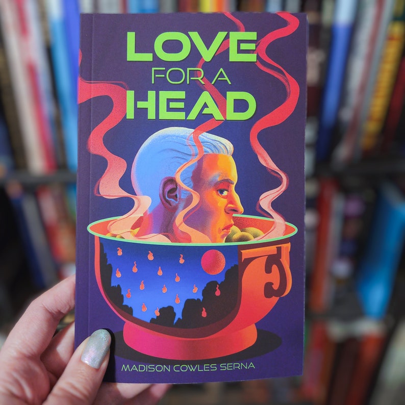 Puede incluir: Una portada de libro con el t&iacute;tulo "LOVE FOR A HEAD" en letras verdes y amarillas. La portada presenta una ilustraci&oacute;n colorida de una cabeza en un taz&oacute;n de sopa.