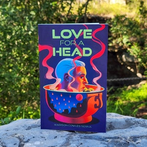 Puede incluir: Una portada de libro con fondo azul y el t&iacute;tulo "LOVE FOR A HEAD" en letras verdes y rojas. La portada presenta una cabeza azul en un taz&oacute;n rojo con vapor saliendo del taz&oacute;n.