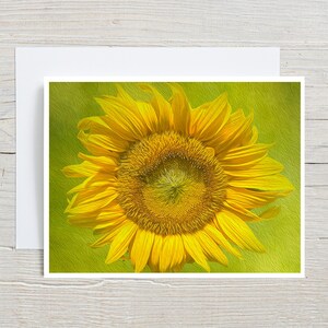 May include: A rectangular greeting card featuring a vibrant yellow sunflower with a textured, painterly effect against a soft lime green background. The sunflower is centered, displaying detailed golden petals and a dark, textured seed head.
