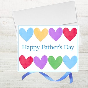 May include: A Father's Day greeting card with a white envelope. The card features eight colorful hearts in blue, yellow, purple, red, and green, with the text "Happy Father's Day" in blue. A blue ribbon is at the bottom.