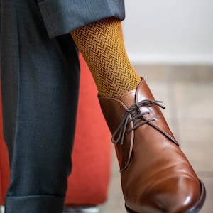 Puede incluir: Un par de botines de cuero marrón con cordones. Los botines se llevan con un par de calcetines de patrón amarillo y marrón.