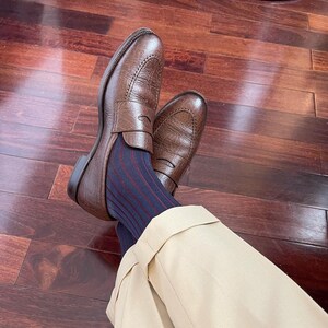 Peut inclure: Mocassins en cuir marron avec une bride &agrave; penny. Les mocassins sont port&eacute;s avec des chaussettes ray&eacute;es bleues et rouges et un pantalon beige.