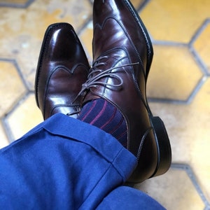 Peut inclure: Une paire de chaussures &agrave; bout aile en cuir marron avec un motif brogue. Les chaussures sont port&eacute;es avec un pantalon bleu et des chaussettes ray&eacute;es.