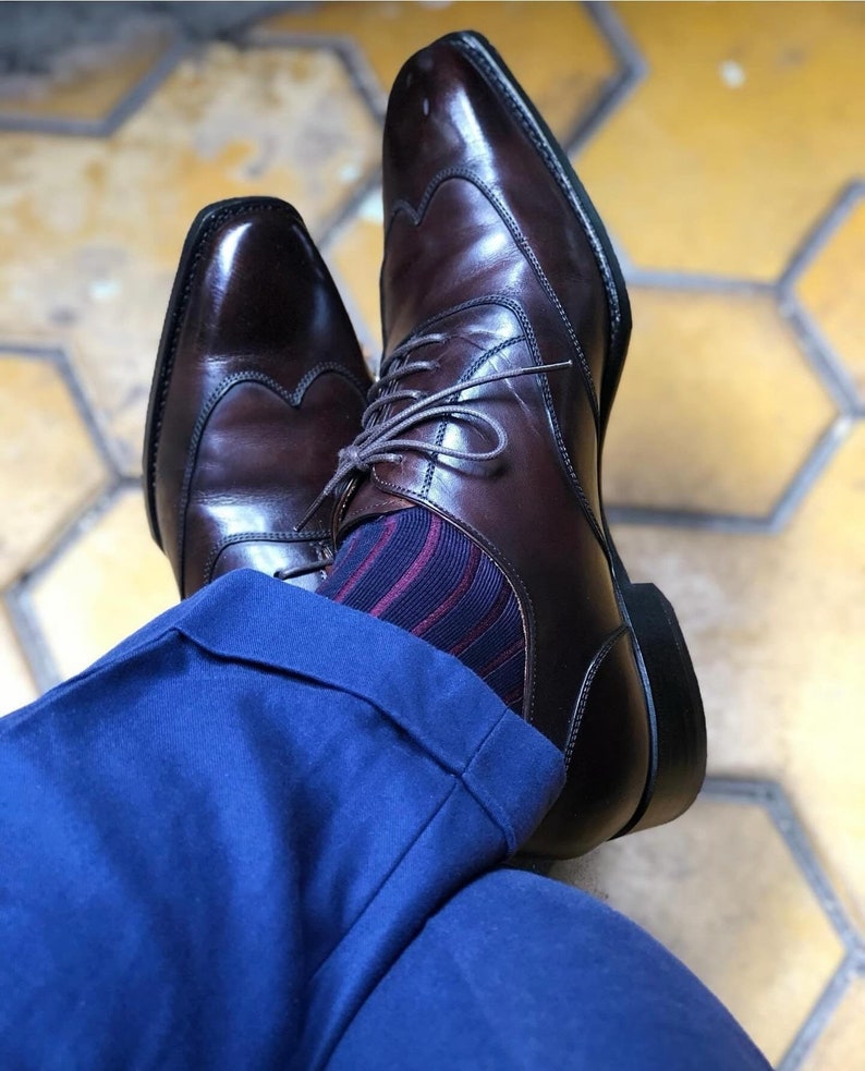 Peut inclure: Une paire de chaussures &agrave; bout aile en cuir marron avec un motif brogue. Les chaussures sont port&eacute;es avec un pantalon bleu et des chaussettes ray&eacute;es.