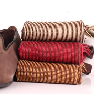 Puede incluir: Una pila de tres corbatas enrolladas con diseños en tonos marrones y rojos, junto a un mocasín de ante marrón. Las corbatas tienen patrones texturizados, una con diseño de rayas y las otras con un pequeño patrón de puntos.