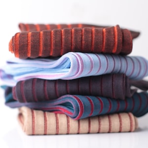 Könnte beinhalten: Ein Stapel aus fünf gestreiften Stoffen, darunter Braun, Blau, Dunkelviolett, Rot und Beige.