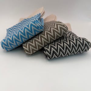 May include: A collection of folded washcloths in various colors, including blue, brown, and black. Each washcloth features a woven chevron pattern. The washcloths have a neutral-colored backing.