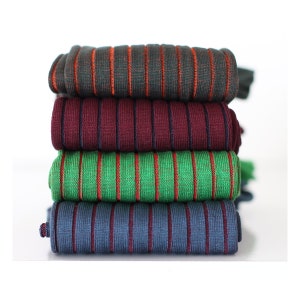 Puede incluir: Una pila de cuatro pares de calcetines a rayas de diferentes colores. Los calcetines están doblados y apilados uno encima del otro. Los colores de los calcetines son verde, burdeos, azul oscuro y un verde oscuro con rayas naranjas.