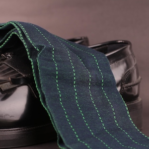 Peut inclure: Une paire de chaussures en cuir noir avec un tissu rayé vert et bleu drapé dessus. Le tissu a un détail de couture verte subtile.