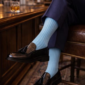 Pode incluir: Mocassins de couro preto com borlas combinados com meias caneladas azul claro. Os sapatos têm um design clássico com um acabamento polido. As meias adicionam um toque de cor ao conjunto.