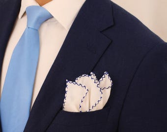 May include: A navy blue suit with a light blue tie and a white dress shirt. A white pocket square with blue stitching is in the suit pocket. The image is a close-up of the suit and tie.