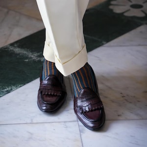 Peut inclure: Une paire de mocassins &agrave; franges en cuir marron. Les mocassins sont port&eacute;s avec des chaussettes ray&eacute;es dans les tons orange, marron et turquoise.