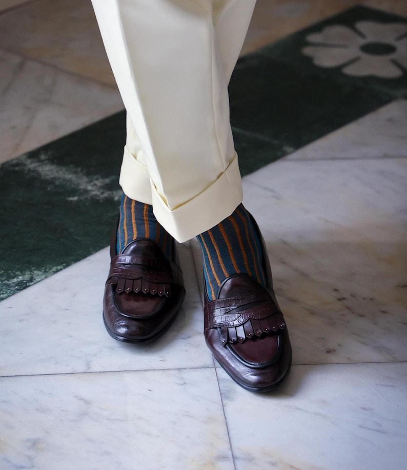 Peut inclure: Une paire de mocassins &agrave; franges en cuir marron. Les mocassins sont port&eacute;s avec des chaussettes ray&eacute;es dans les tons orange, marron et turquoise.