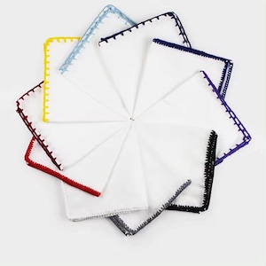 Könnte beinhalten: Ein Set aus acht weißen Taschentüchern mit verschiedenen farbigen Häkelrändern. Die Farben umfassen Gelb, Rot, Blau, Lila, Schwarz und Grau.